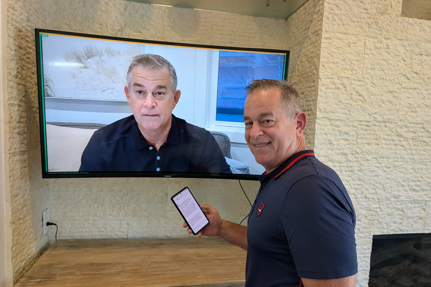 Ed Zanelli beside a TV showing the SeniorMinder avatar, holding a phone with a caregiver alert